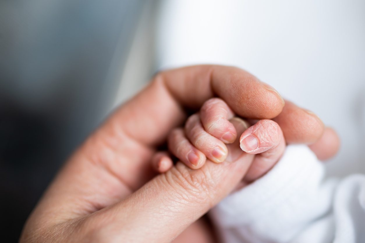 A newborn holding an adult’s finger